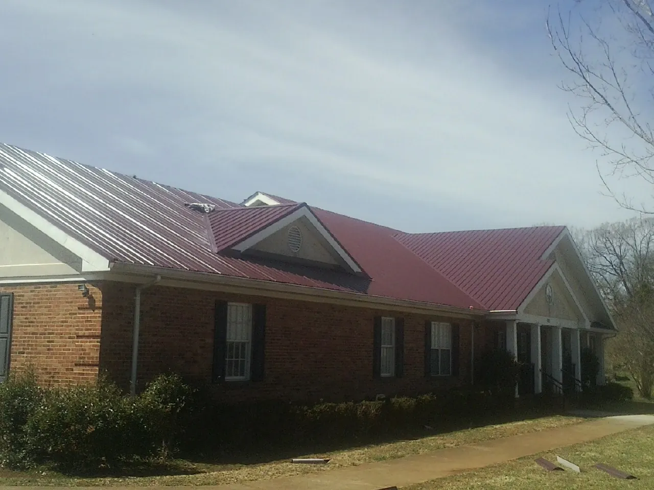 Red metal roof with gabled entries on a long brick building, from a Hail Damage Roof Repair job in Hadley